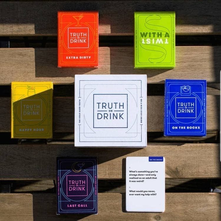 Truth or Drink card game boxes in various colors on a wooden table.