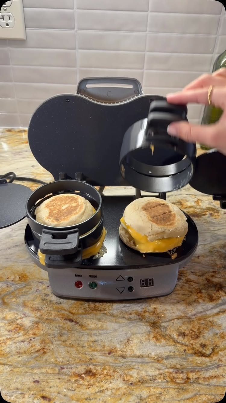 Breakfast sandwich maker on a counter with two toasted cheese sandwiches inside.