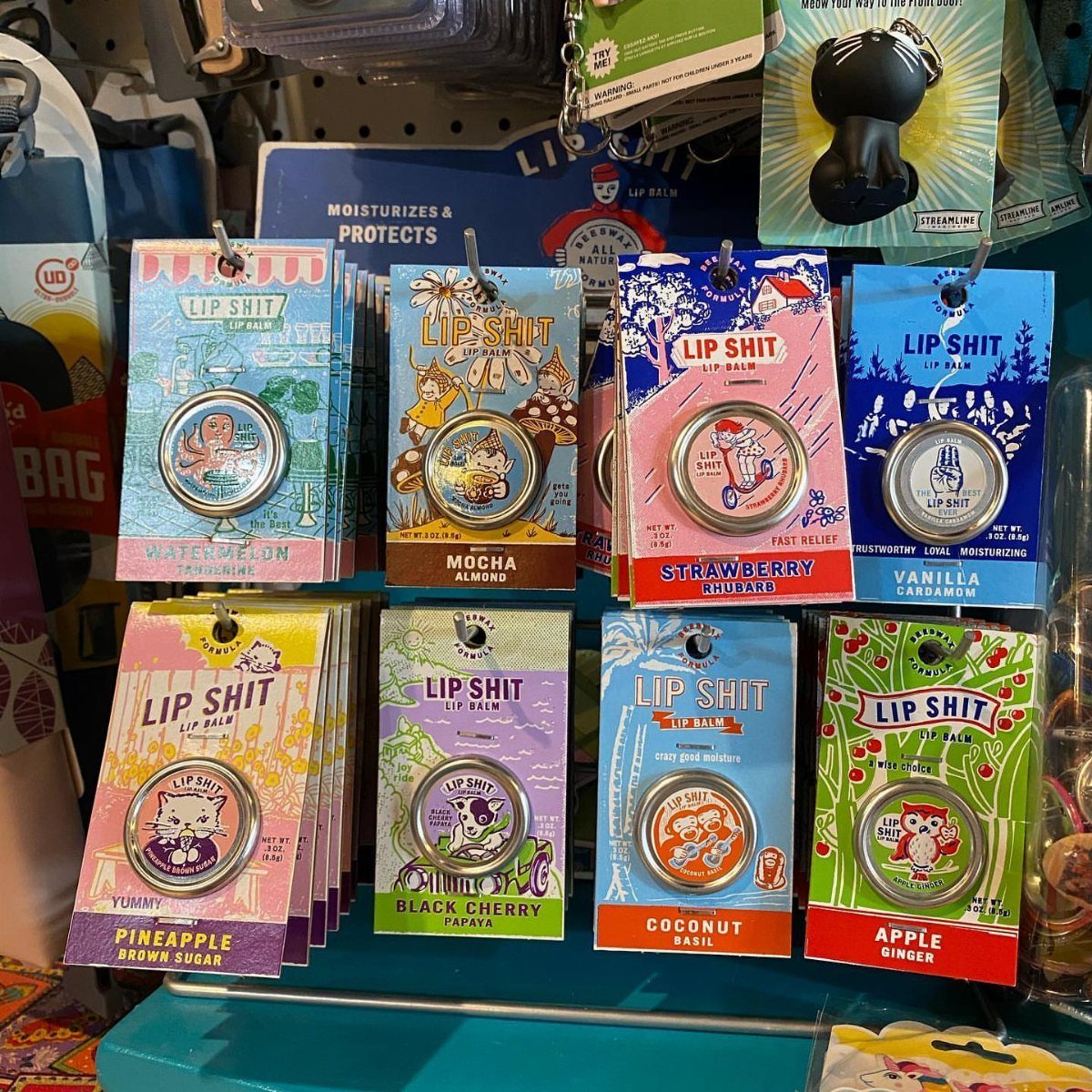 Assorted Lip Shit lip balm tins with colorful packaging on a store shelf.