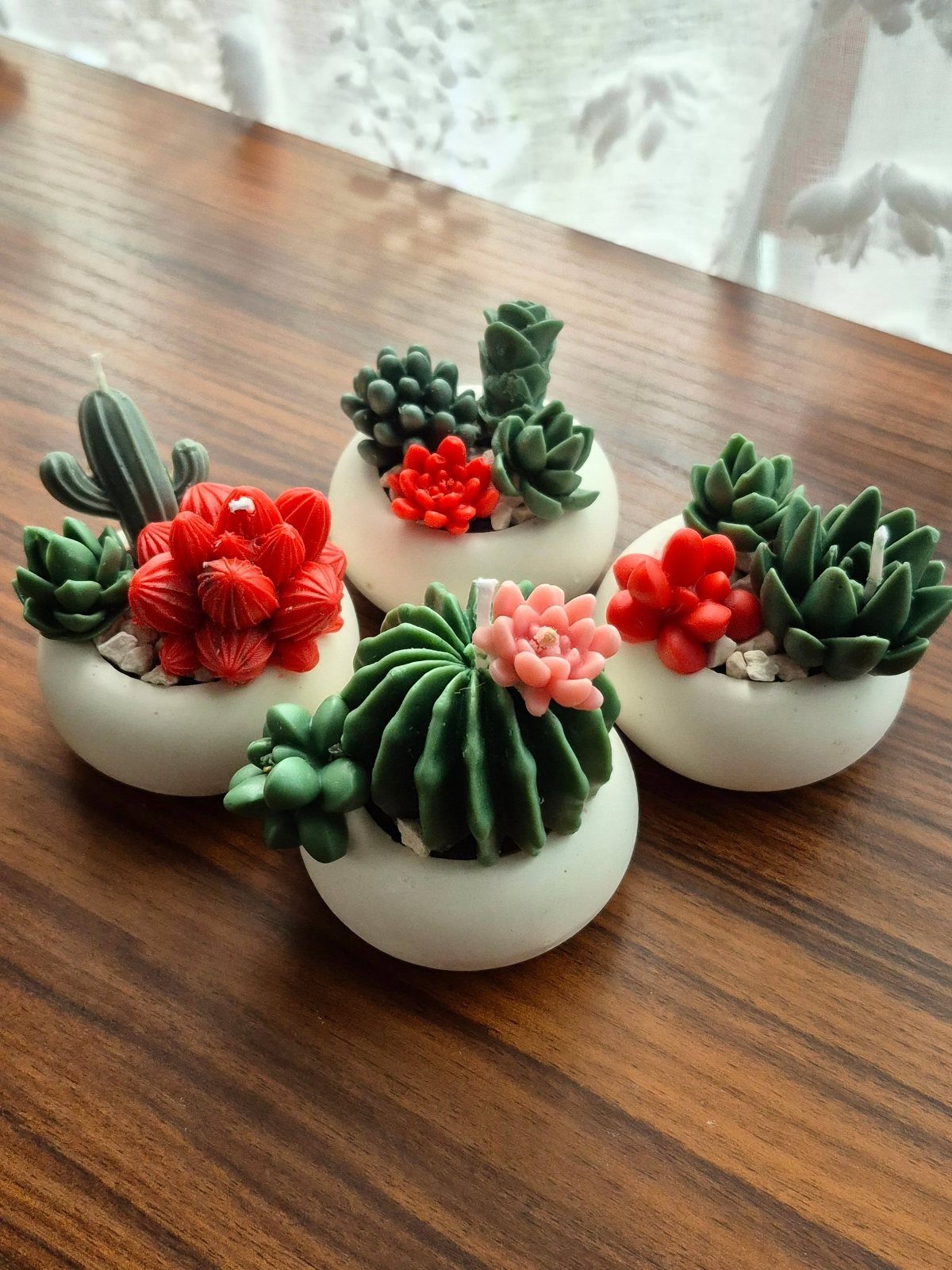 Four mini succulent candles in white pots on a brown wooden table.