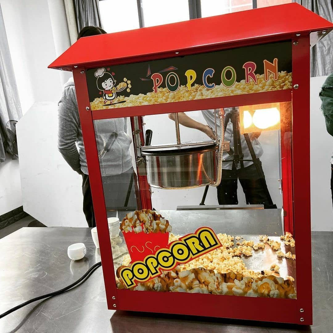 Red tabletop popcorn machine filled with popped corn on a metal counter.