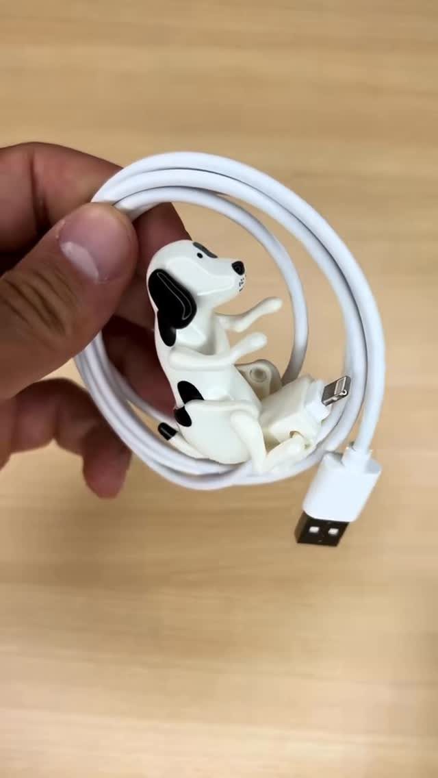 White USB charging cable with a small spotted dog figure held in a hand.