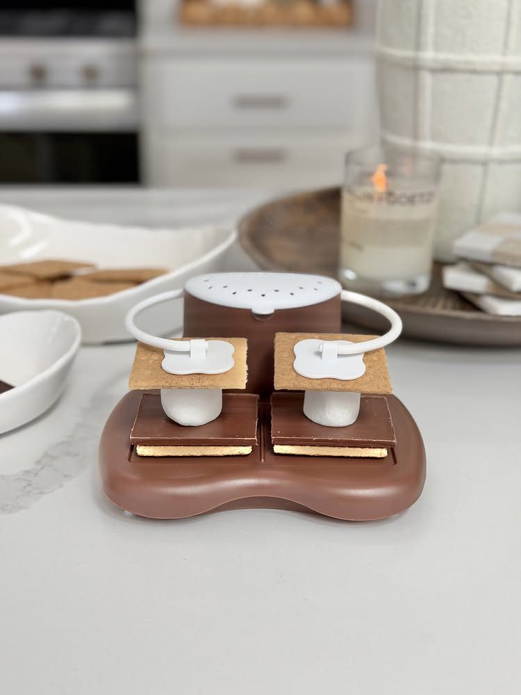 Brown chocolate-shaped s'mores maker with graham crackers and marshmallows on a white counter.