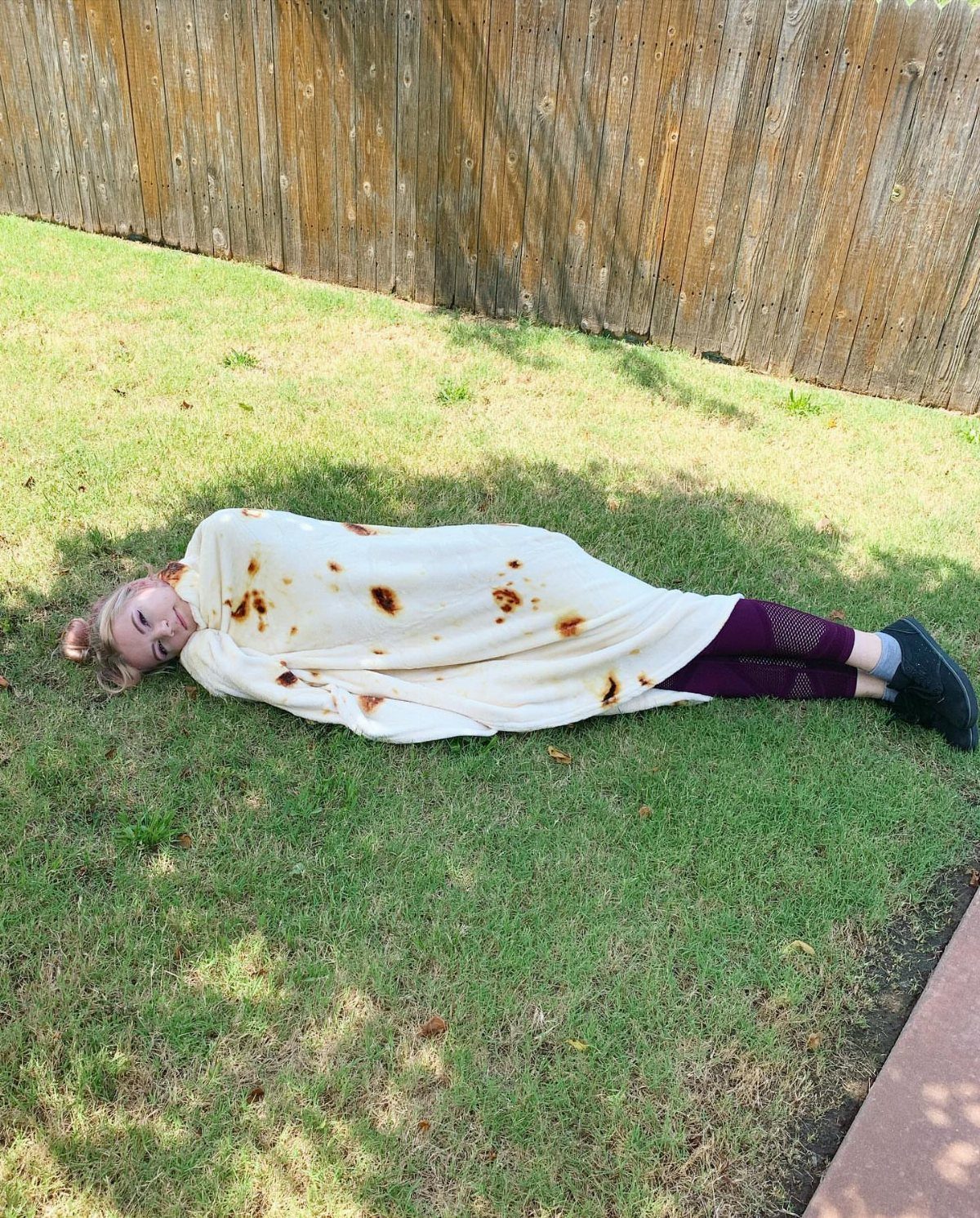 Person wrapped in a tortilla burrito blanket lying on a green lawn