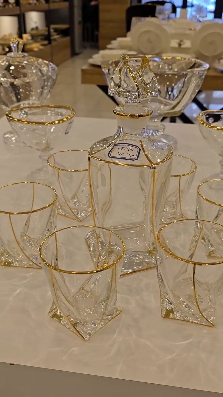 Glass decanter and tumblers with gold rims on a white marble surface.