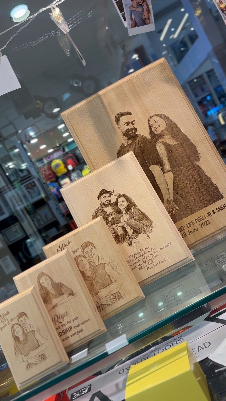 Laser-engraved wooden plaques featuring portraits of couples displayed on a glass retail shelf.