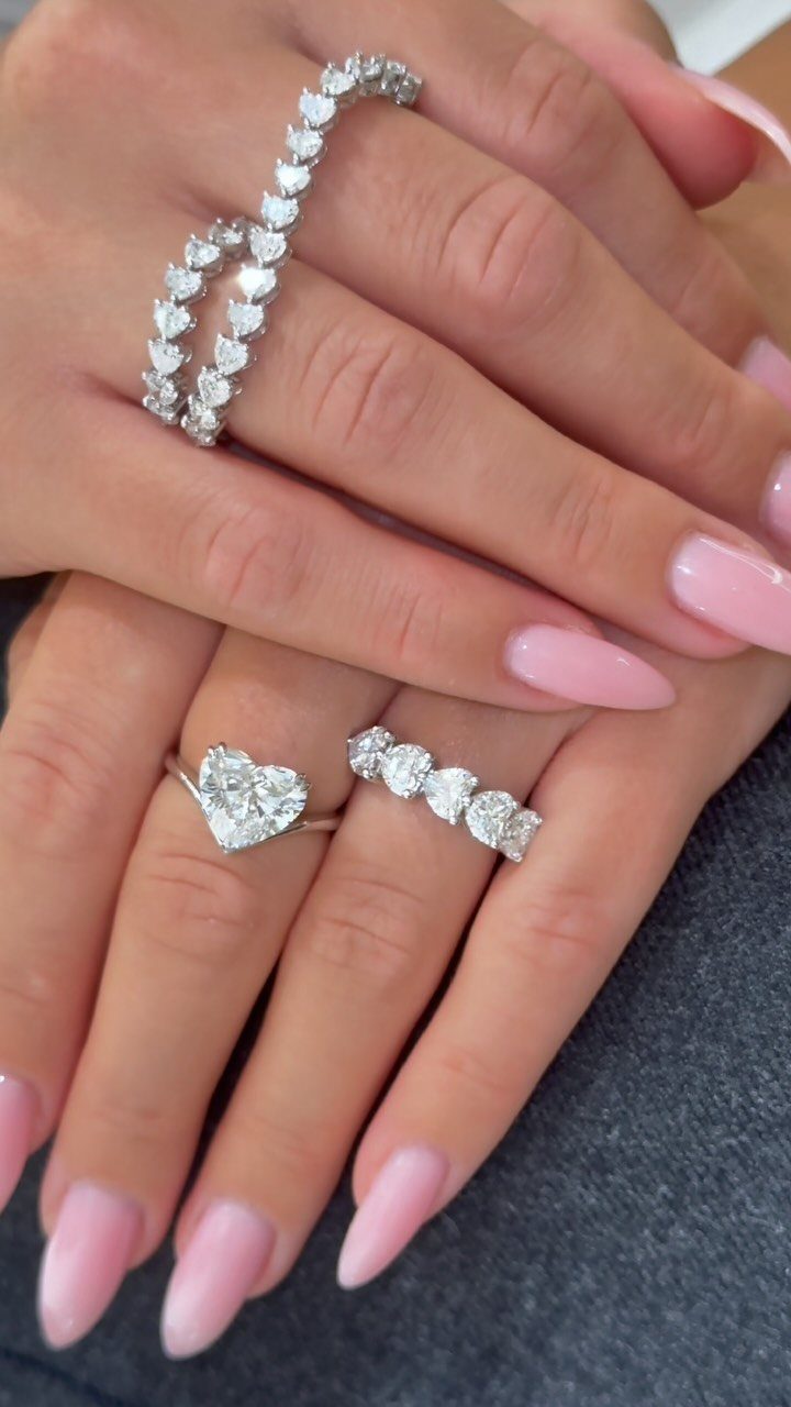 Diamond rings including a heart-shaped stone on fingers with pink manicured nails.