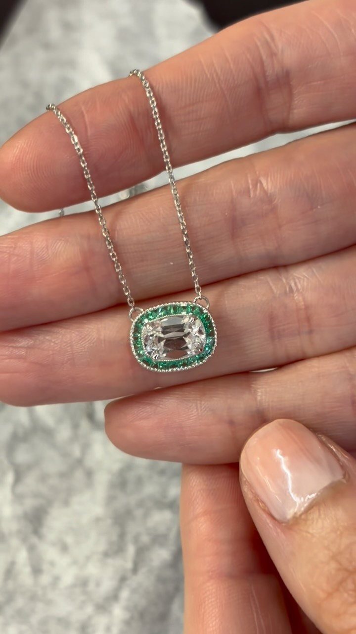Silver necklace with an oval clear gemstone surrounded by small green emeralds.
