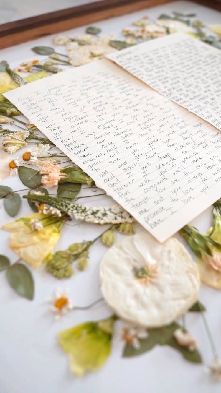 Handwritten letters surrounded by pressed dried flowers and leaves in a wooden frame.