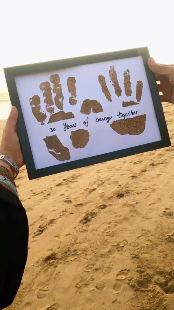 Framed artwork with brown handprints and 30th anniversary text held on a beach.