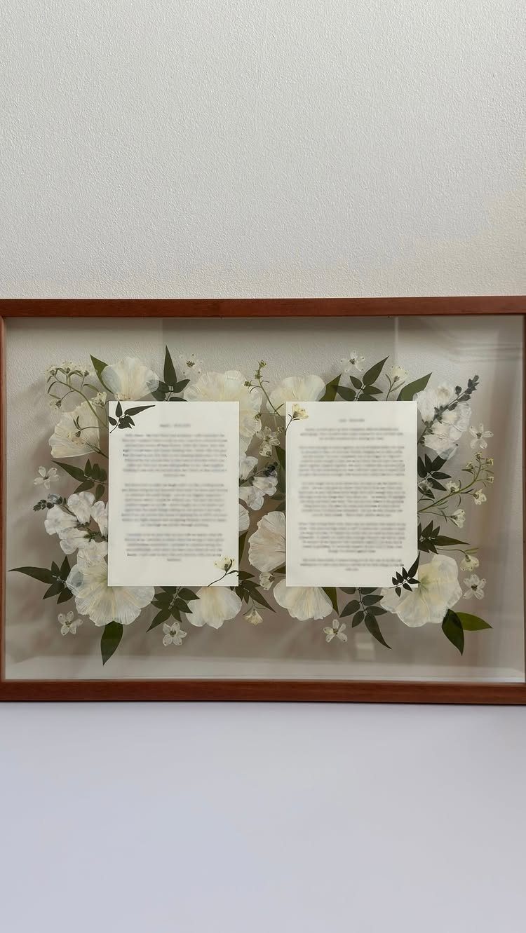 Framed wedding vows and white flowers preserved in a wooden shadow box.