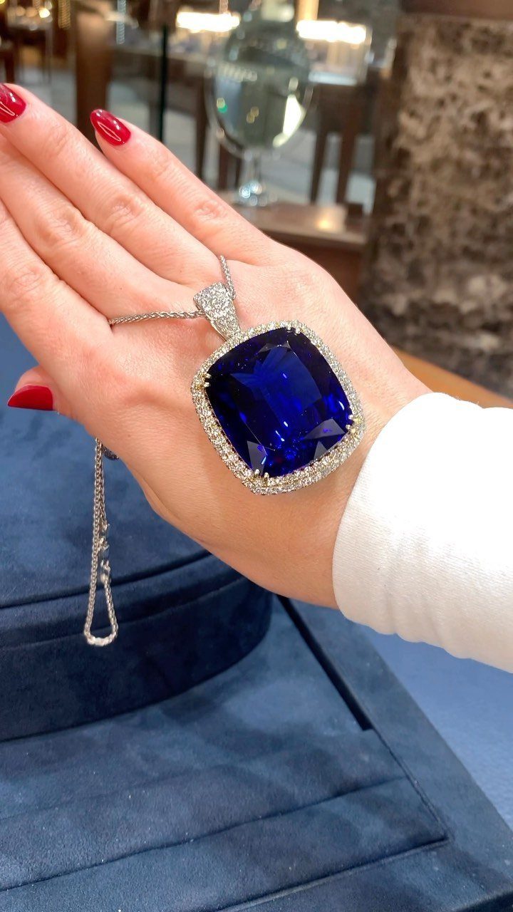 Large blue sapphire pendant with diamond halo held in a hand over blue velvet